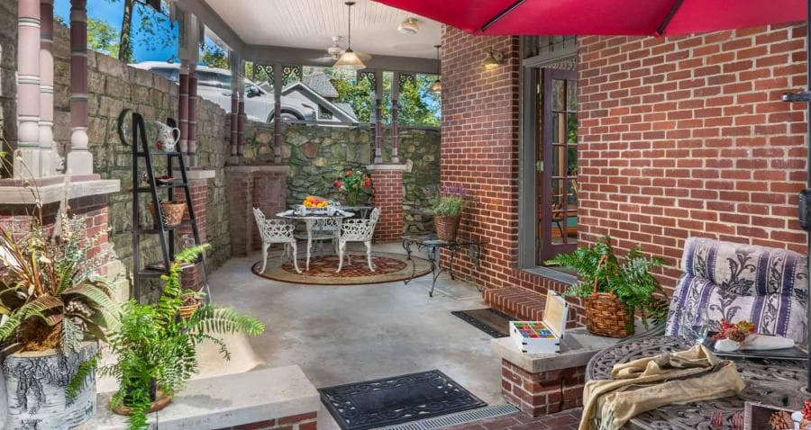 A cozy outdoor patio featuring a round table, chairs, and lush plants under a red umbrella.
