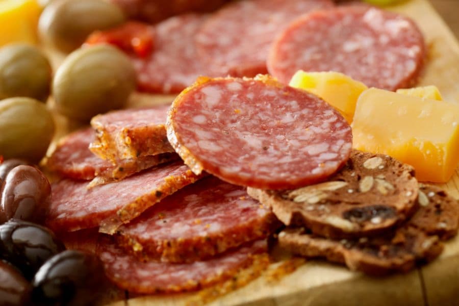 A close-up of assorted meats, olives, and cheese arranged beautifully on a wooden platter.