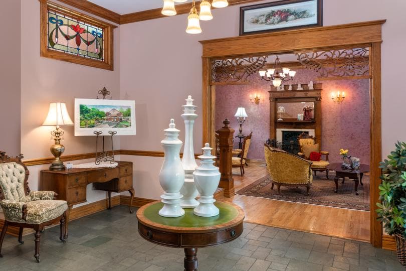 A warmly decorated entryway featuring a table with decorative vases, a lamp, and an arched doorway leading into a cozy sitting room.