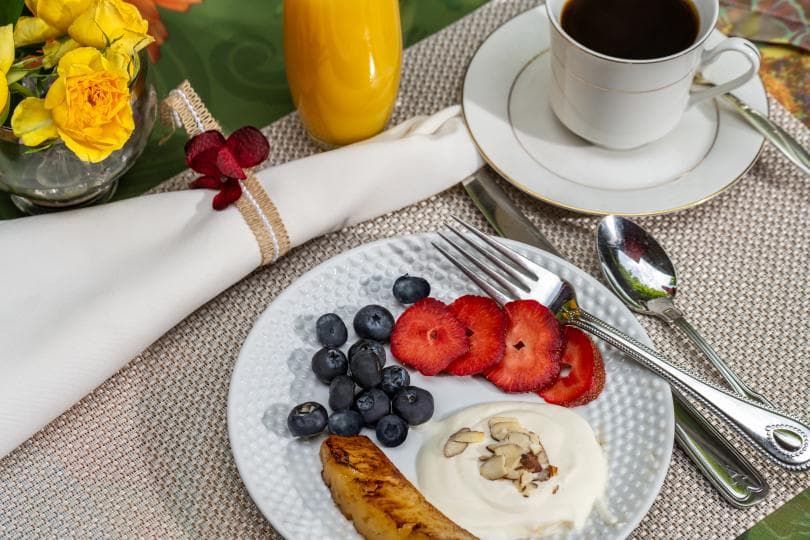 A breakfast plate with yogurt, strawberries, blueberries, and a banana, accompanied by coffee and orange juice, on a elegantly set table.