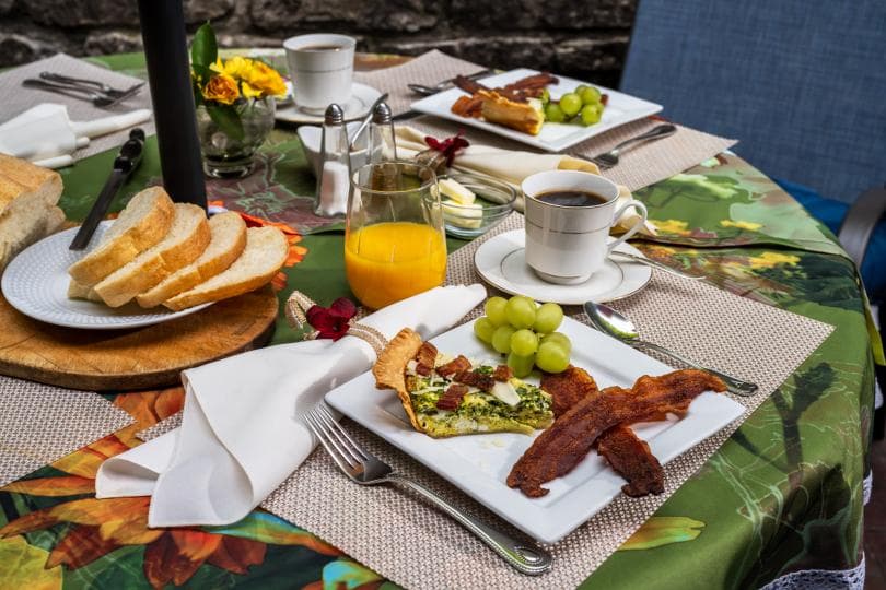 A beautifully arranged breakfast table featuring eggs, bacon, toast, grapes, juice, and coffee.