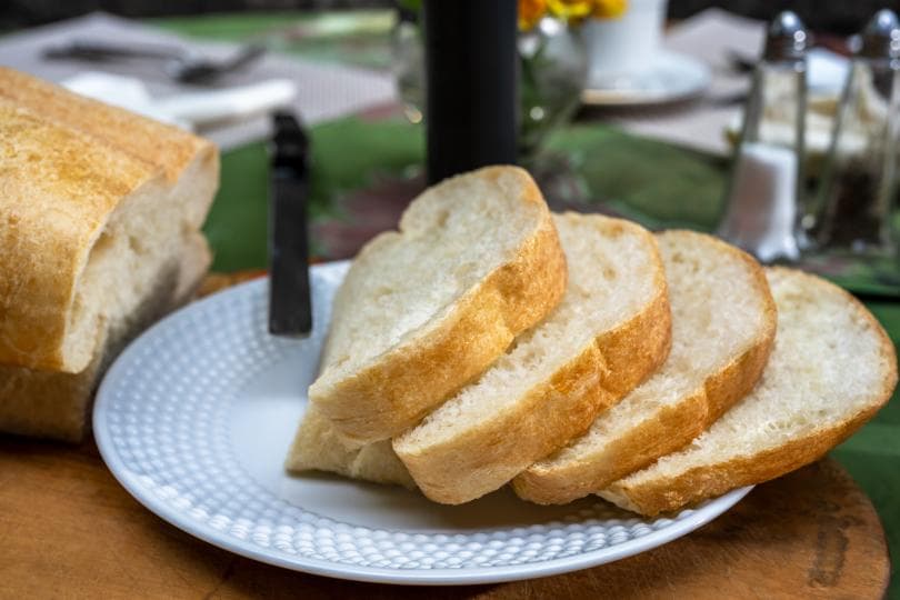 Sliced bread arranged on a plate next to a whole loaf.