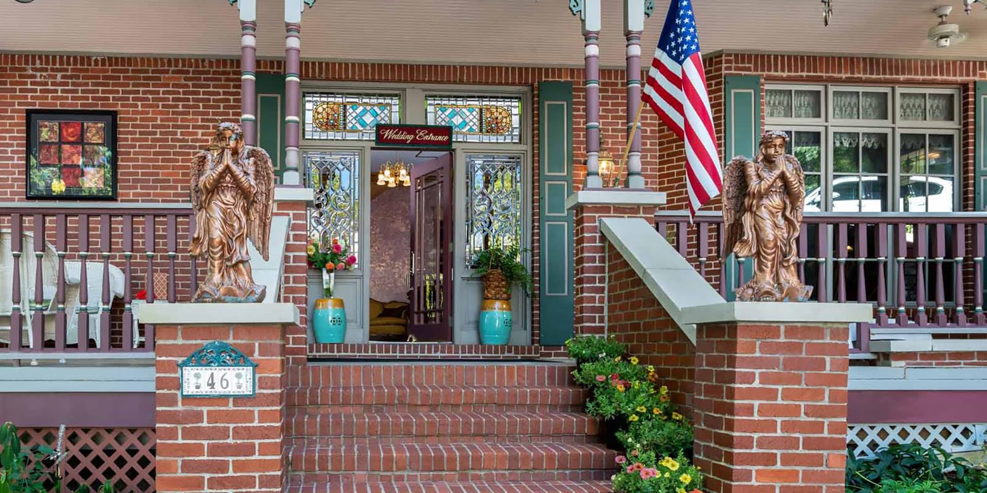 A charming brick porch featuring angel statues, potted plants, and a decorative entrance with stained glass.