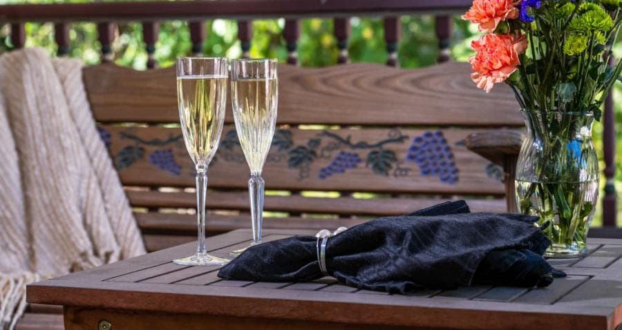 Two champagne flutes on a wooden table beside a black napkin and a vase of colorful flowers.