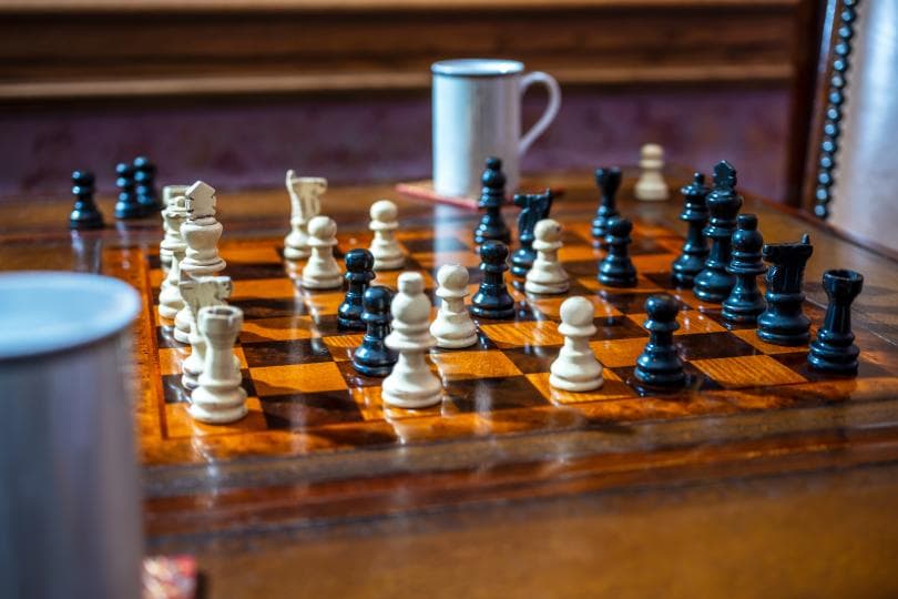 A chessboard with black and white pieces, accompanied by a coffee mug.