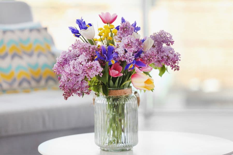 A vibrant bouquet of assorted flowers in a glass jar on a table.