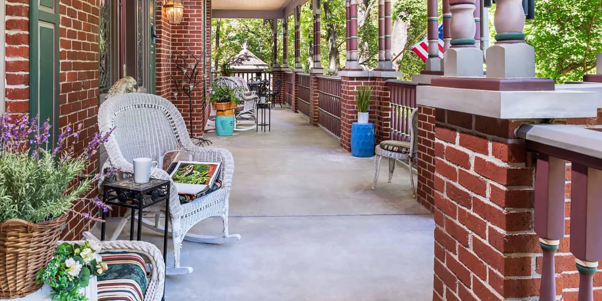 A charming porch featuring wicker furniture, potted plants, and a peaceful, wooded backdrop.
