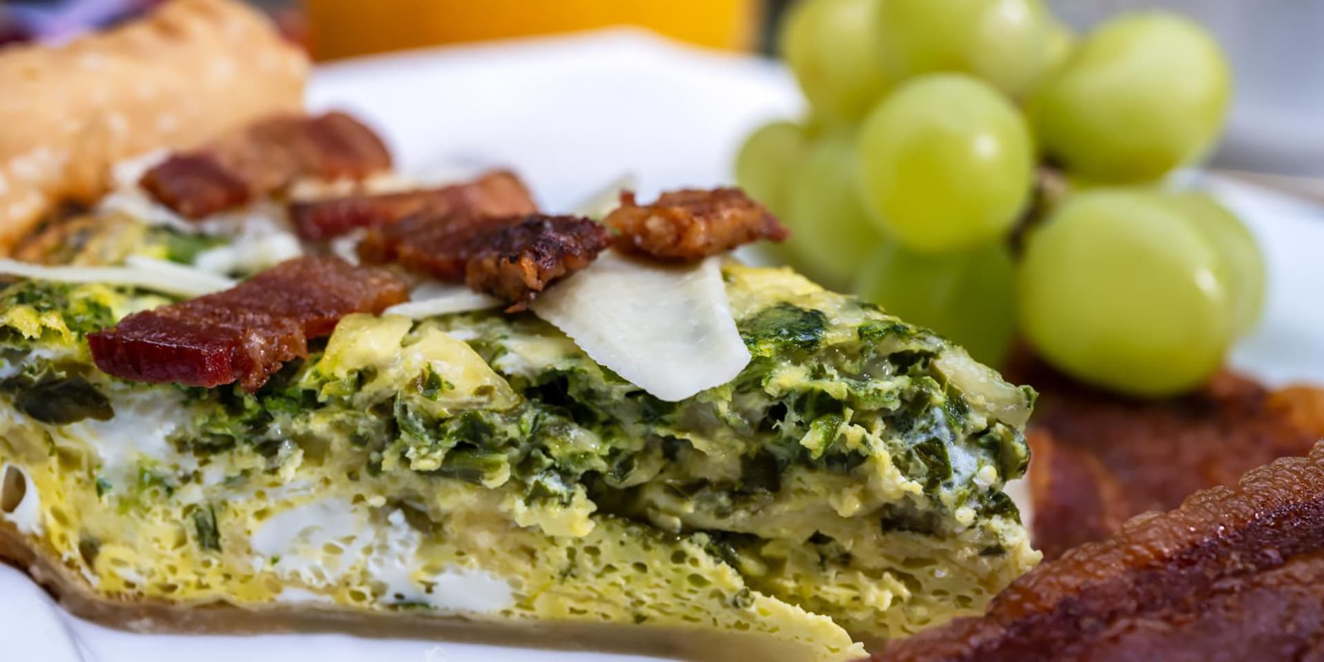 A slice of spinach and bacon frittata served with green grapes and a side of pastry.